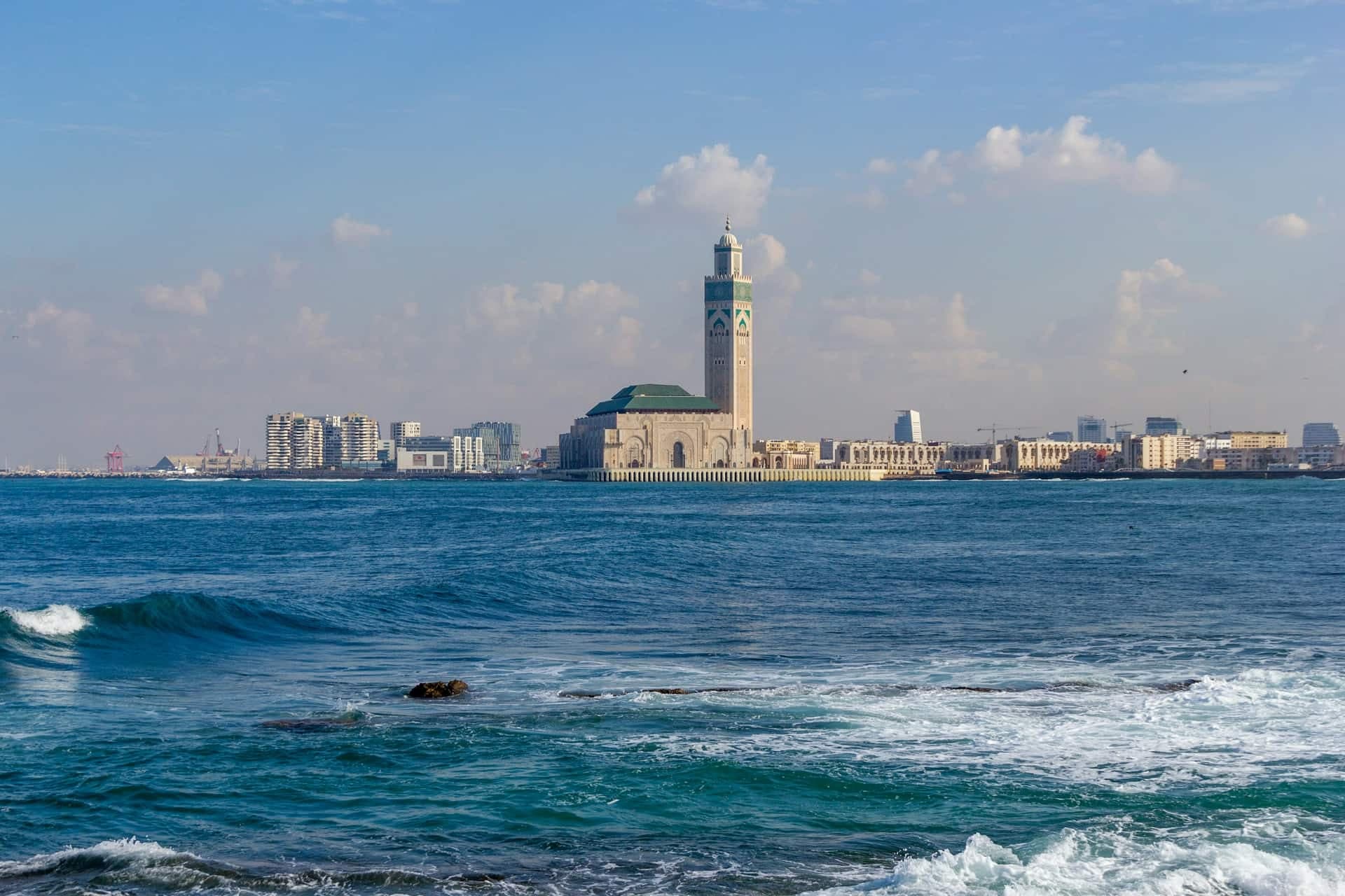 The Hassan II Mosque and its tall minaret seen across the Atlantic from the Casablanca shoreline, with apartment blocks along the coast.