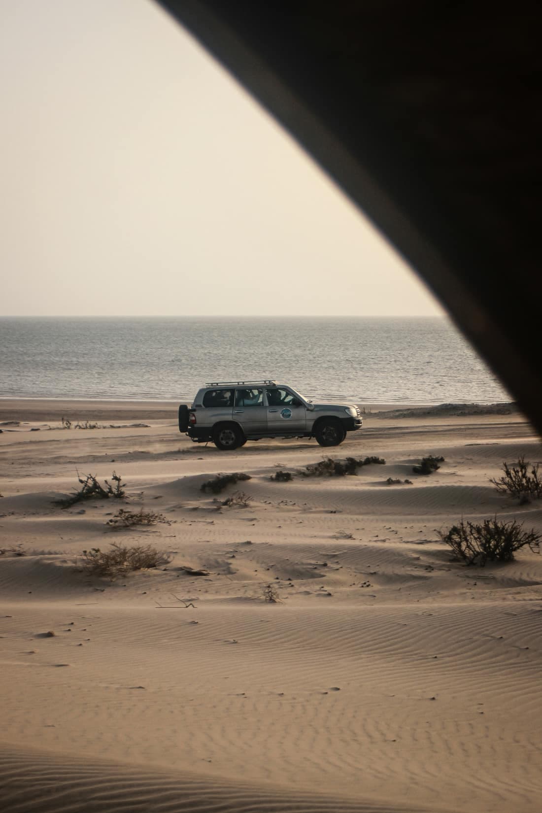 An off-road vehicle crossing the sandy shore at Dakhla, with low dunes and the calm sea behind it.