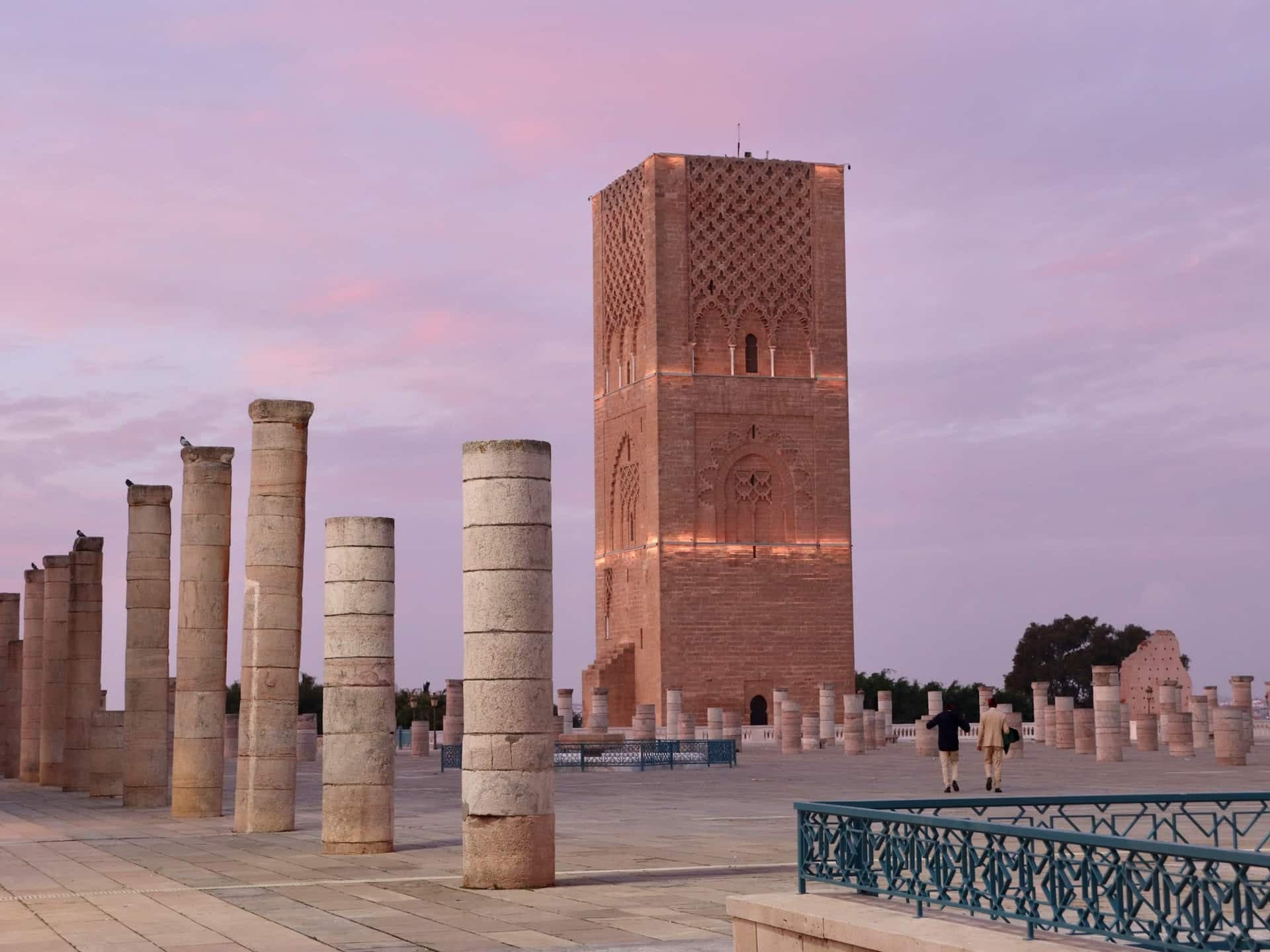 The unfinished Hassan Tower in Rabat at dusk, with rows of stone column bases standing on the esplanade in front of it.
