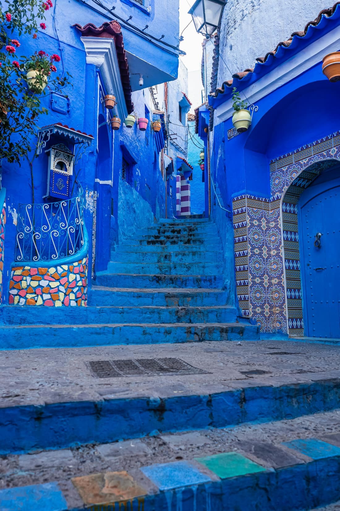A stepped blue alley in the Chefchaouen medina, with tiled walls, a painted door and wrought-iron railings.