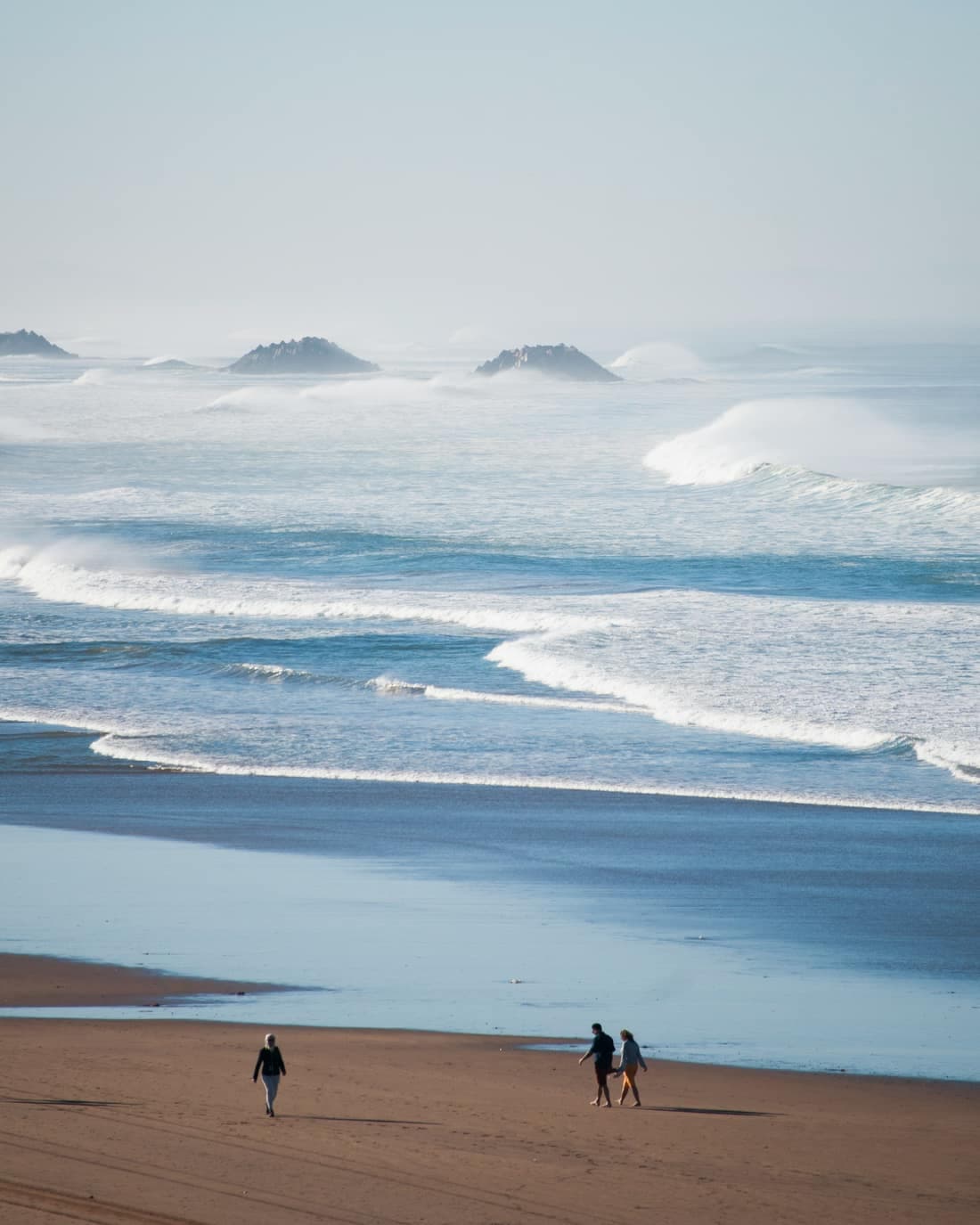 Atlantic waves rolling onto a wide beach near Agadir, with rocky headlands in the sea mist behind.