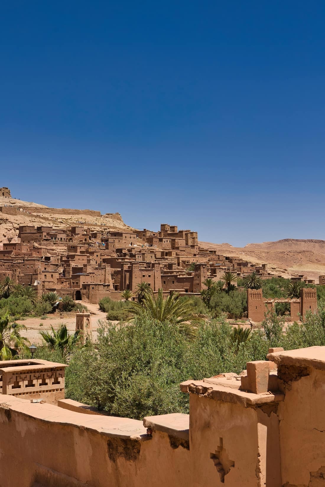The earthen village of Aït Ben Haddou spread along the hillside above palm trees and desert scrub.