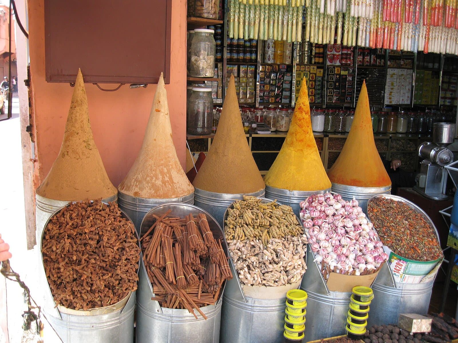 Tall cones of ground spices above tubs of cinnamon bark, dried rosebuds and other spices at a shop front in the Marrakech medina.