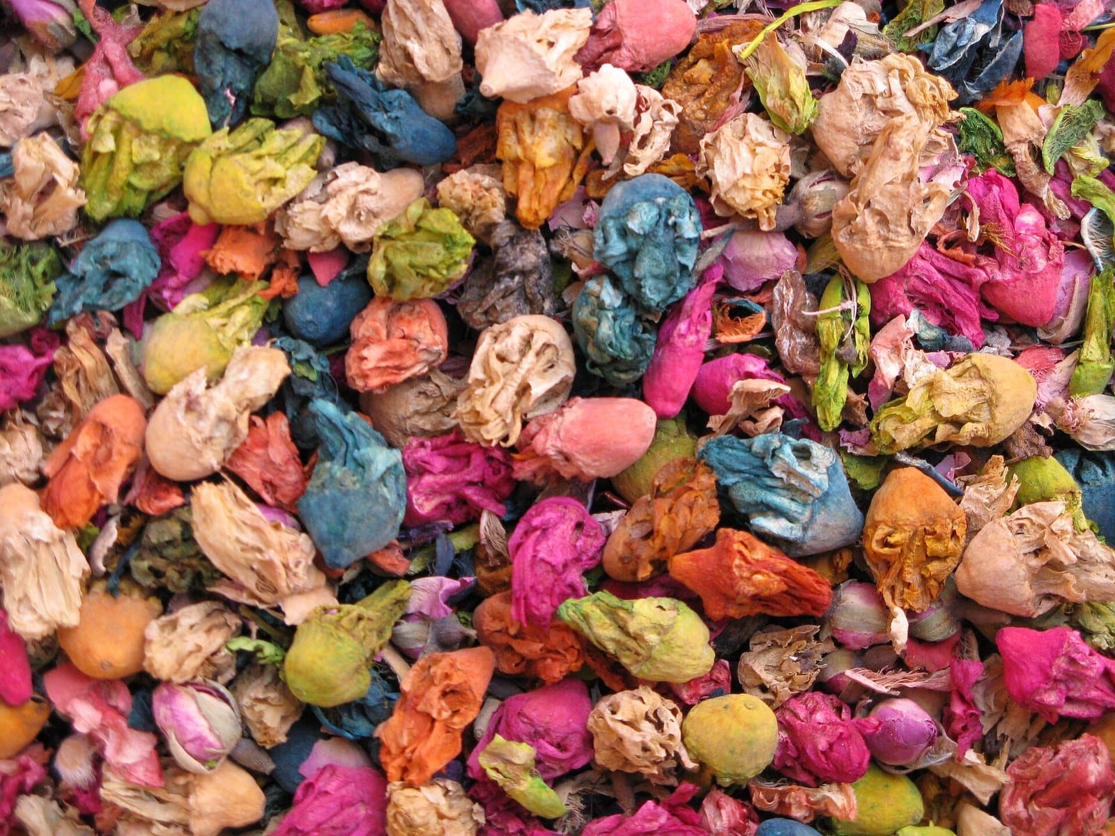 A close-up of dyed pot-pourri and dried flower buds in pink, blue, yellow and green, piled high at a Marrakech spice market stall.
